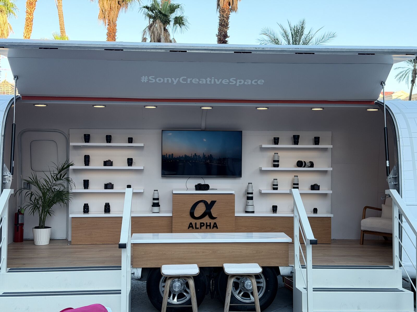 Professional mobile creative space or product showcase with camera equipment display and palm trees visible in a clean minimalist setup